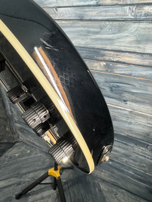 Close-up of a black guitar with a white pickguard on a wooden surface