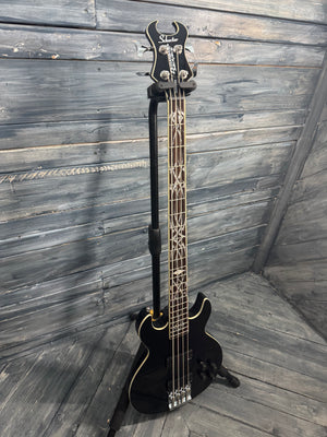Black electric bass guitar on a stand against a wooden wall.
