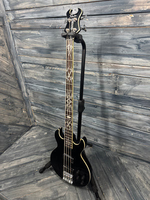 Black electric bass guitar leaning against a wooden wall.