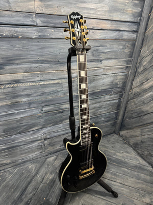 Black electric guitar on a stand against a wooden wall.