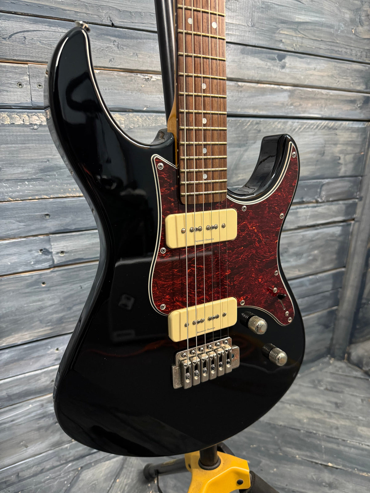 Black electric guitar with a red pickguard on a wooden surface