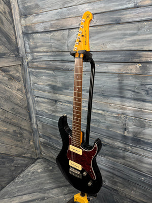 Black electric guitar with a yellow pickguard on a wooden background