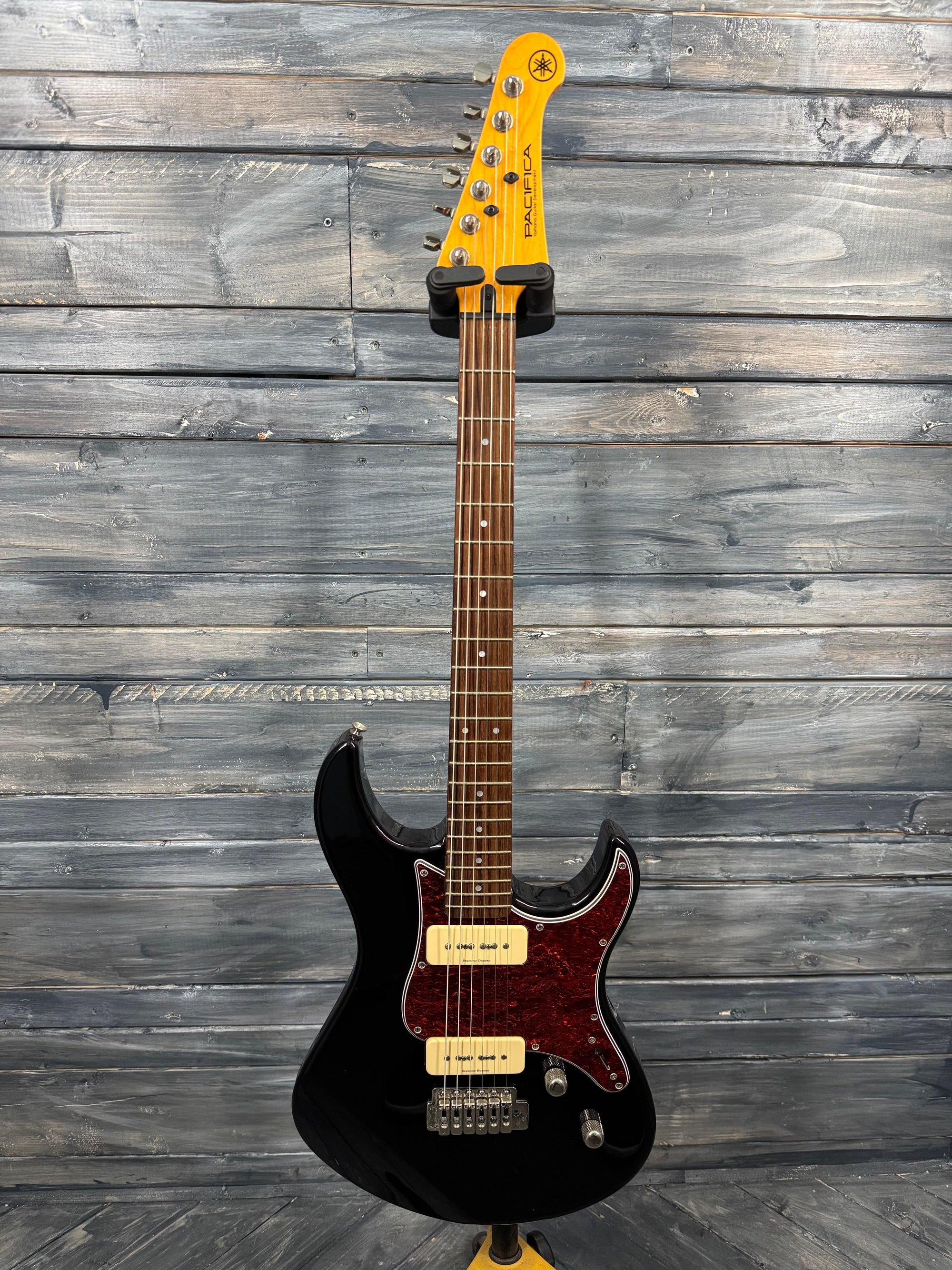 Electric guitar with a black body and yellow neck against a wooden background