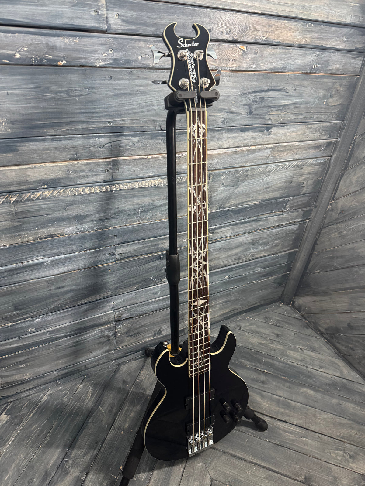 Black electric bass guitar on a stand against a wooden wall.