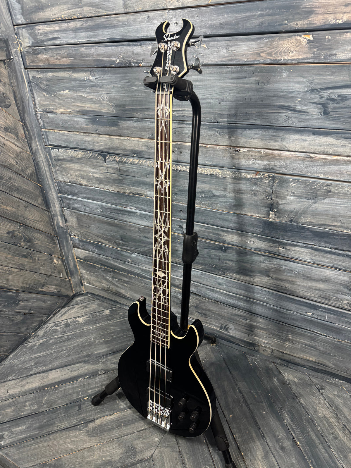 Black electric bass guitar leaning against a wooden wall.