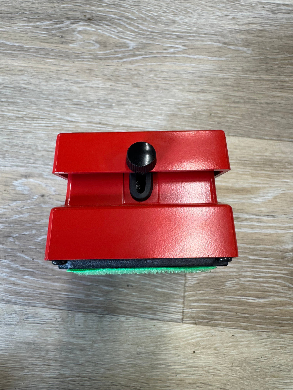 Red cleaning tool with a black brush on a wooden surface