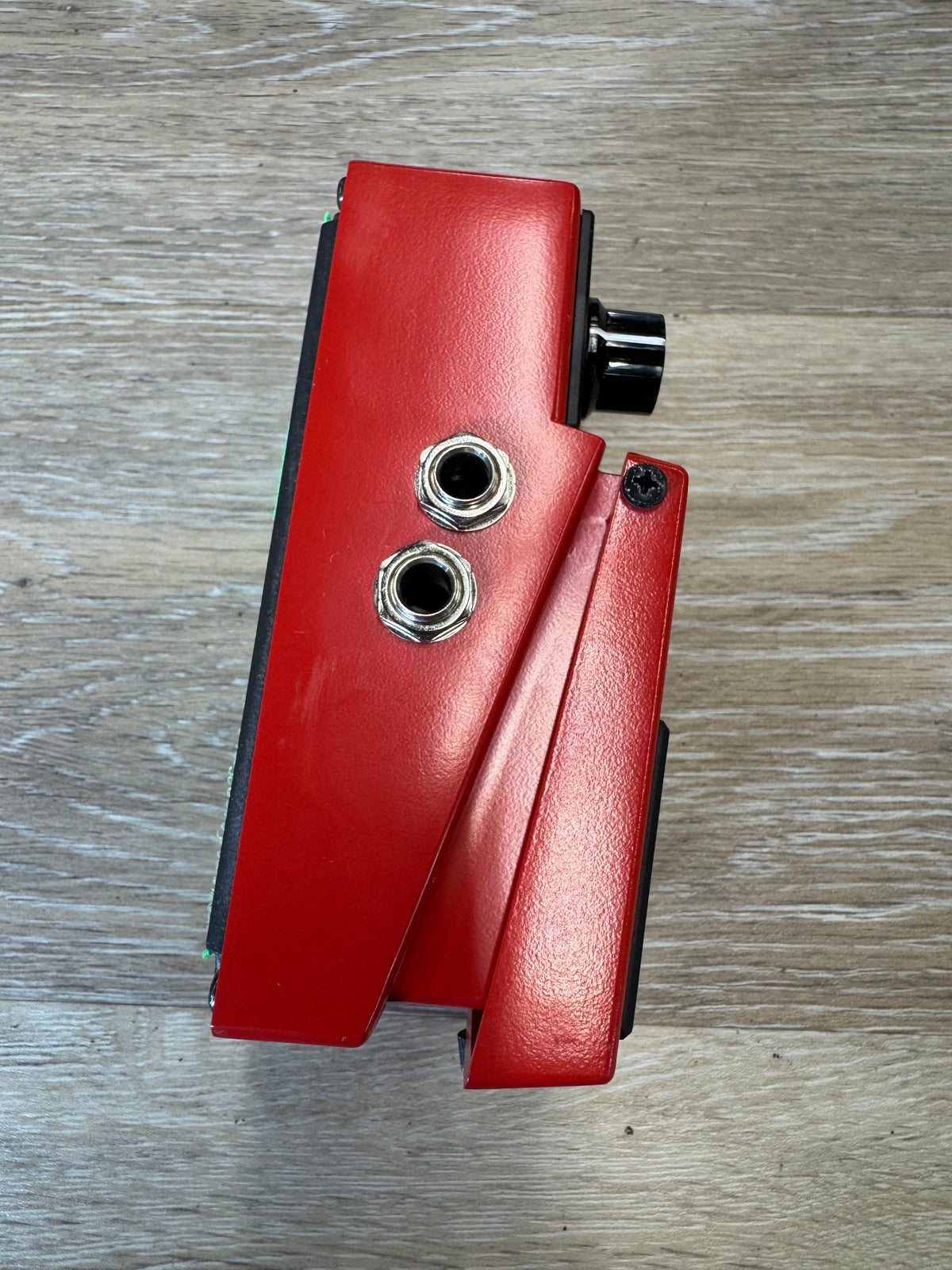 Red guitar pedal with two metal jacks on a wooden surface