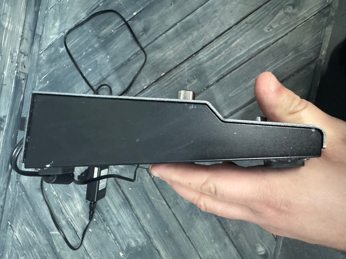 Hand holding a black electronic device against a wooden background