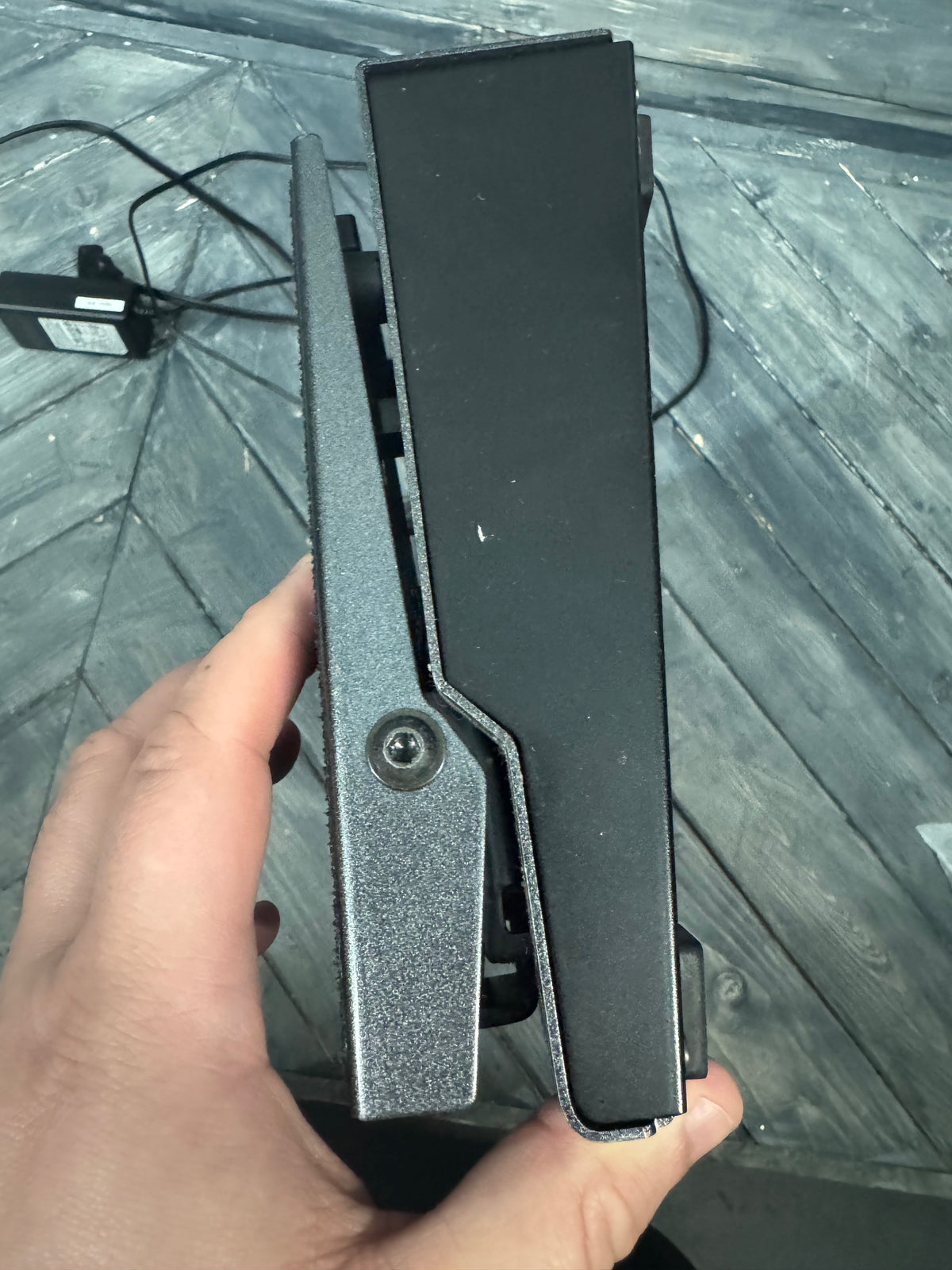 Hand holding a black electronic device on a wooden surface