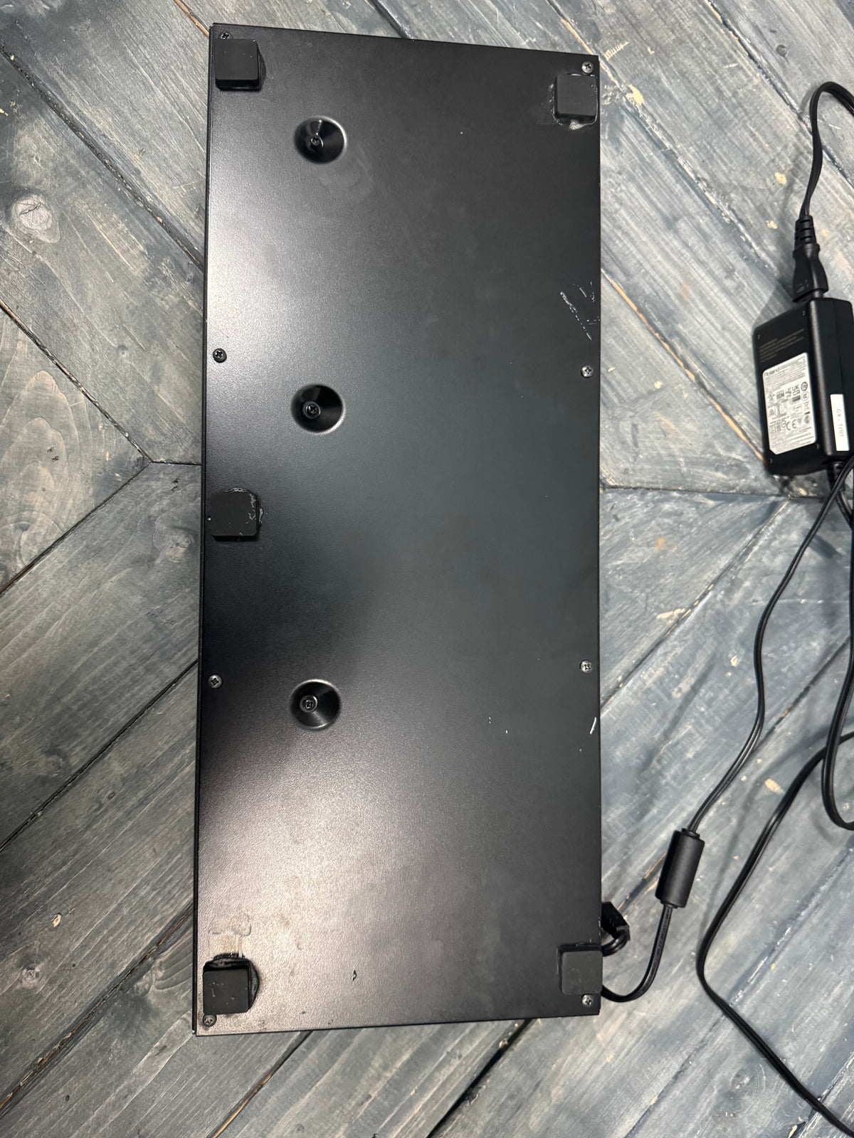 Black rectangular object with multiple holes on a wooden surface