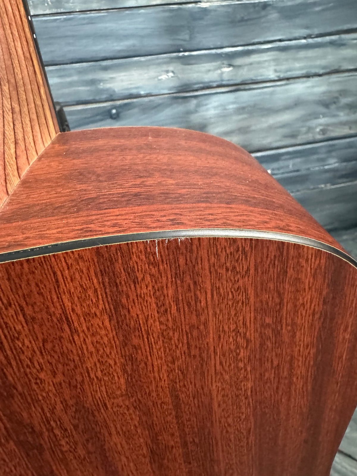Close-up of a wooden guitar with a metal truss rod, against a rustic wooden background.