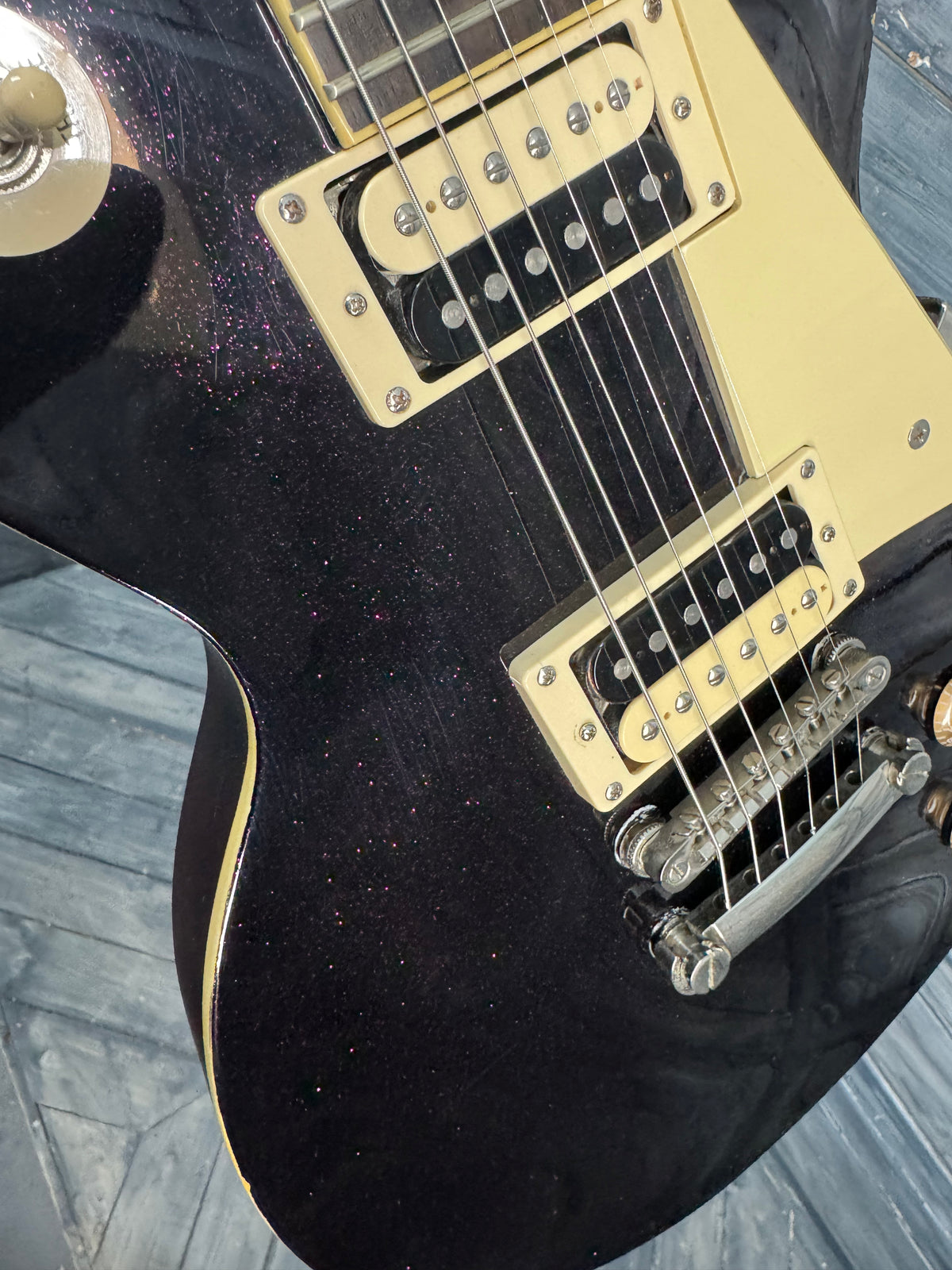 Close-up of a black electric guitar with gold hardware on a wooden surface