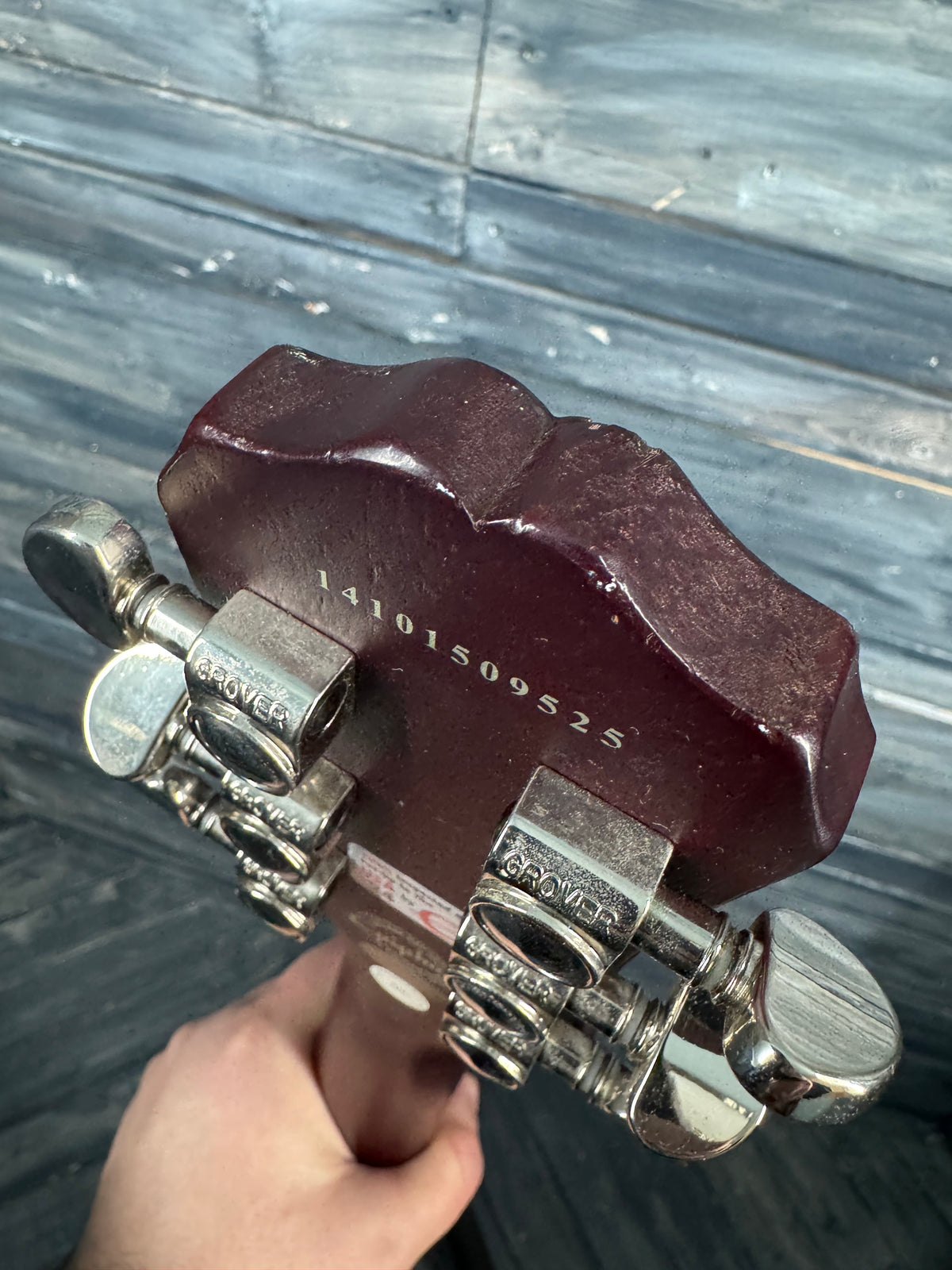 Maroon guitar capo held by a hand on a wooden floor background