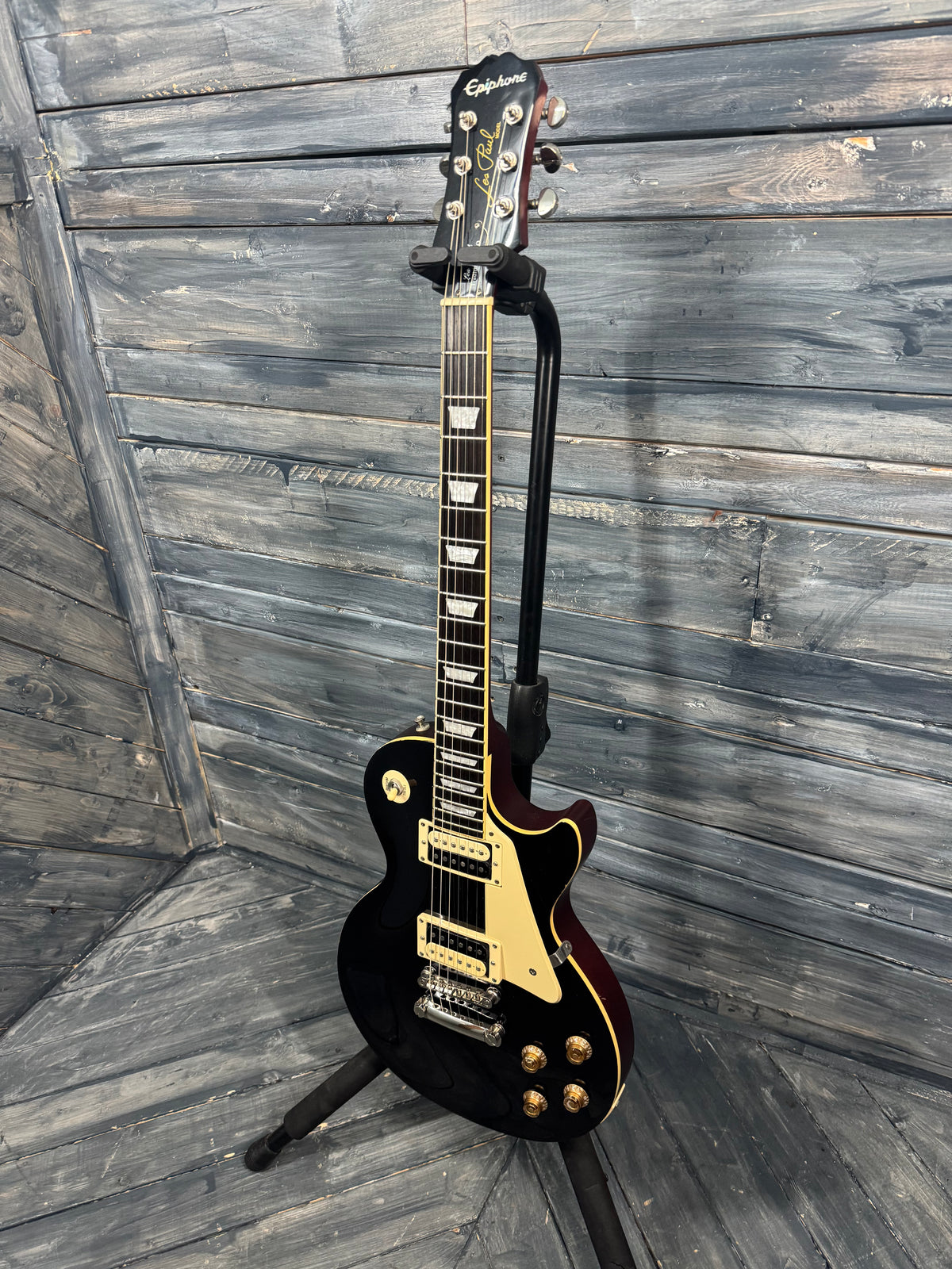 Black electric guitar on a stand against a wooden wall.