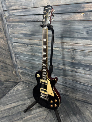 Black electric guitar on a stand against a wooden wall.