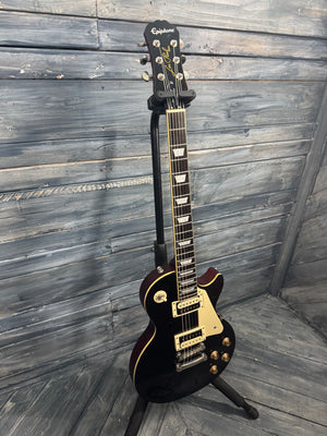 Black electric guitar on a stand against a wooden wall