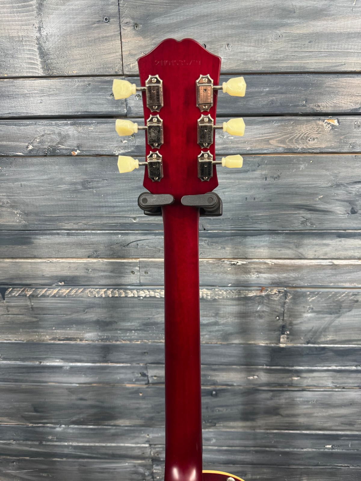 Red guitar neck with tuning pegs against a wooden background