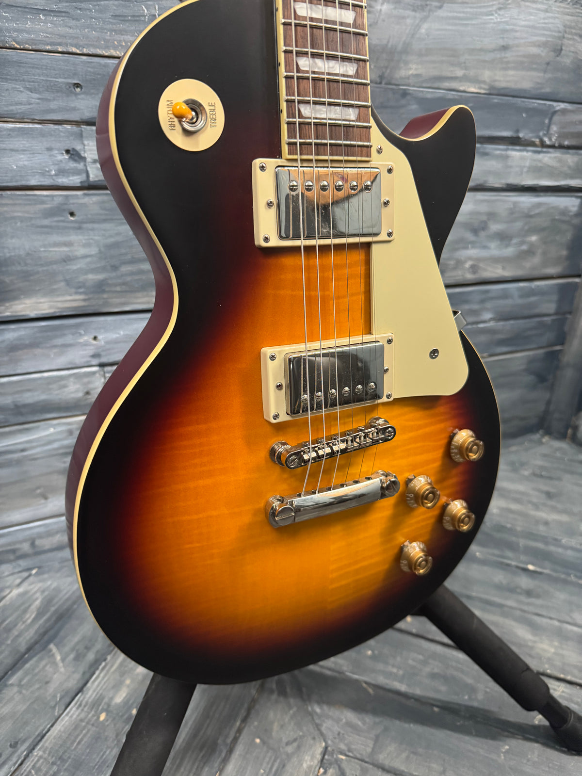 Electric guitar with a sunburst finish on a wooden stand against a wooden wall.