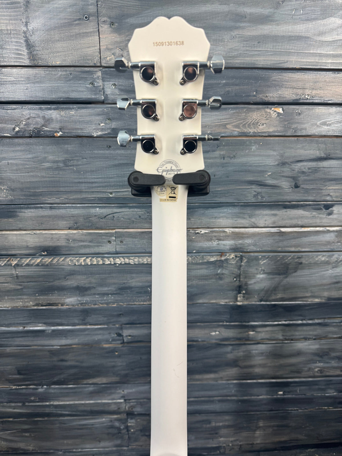 White guitar neck with tuning pegs on a wooden surface