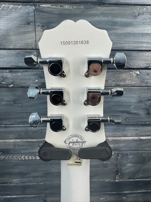 Close-up of a white guitar headstock with tuning pegs against a wooden background