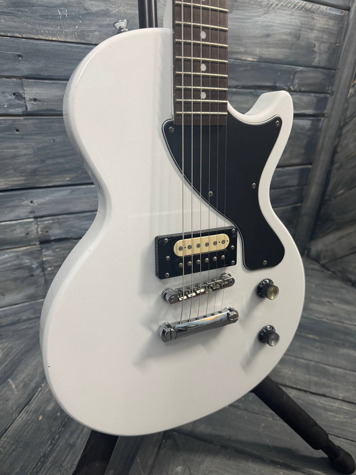 White electric guitar with black pickguard on a wooden surface