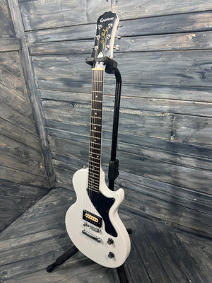 White electric guitar on a stand against a wooden wall