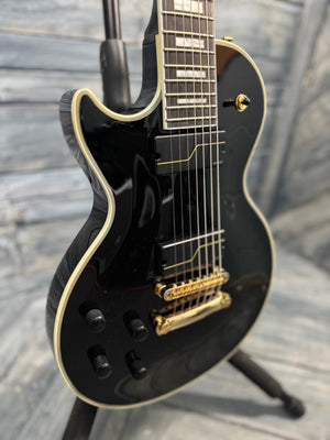 Black electric guitar with gold hardware on a wooden floor