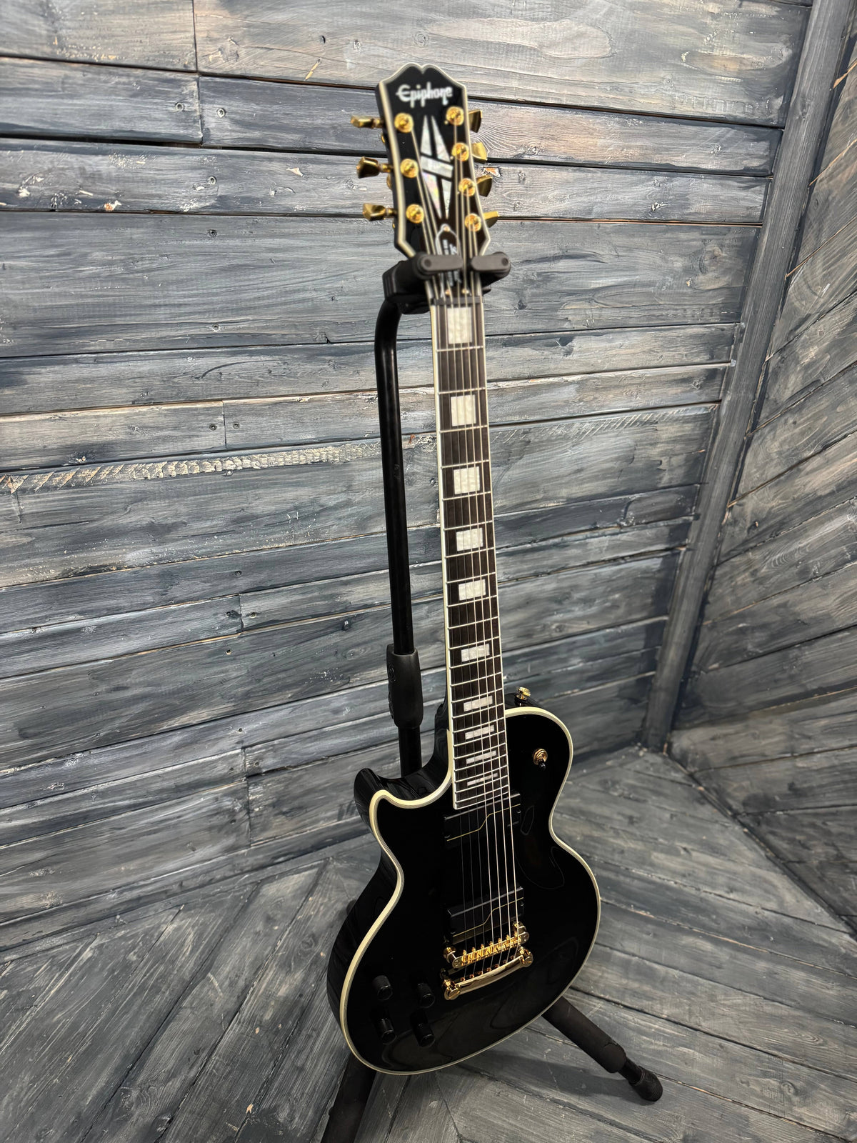 Black electric guitar on a stand against a wooden wall.
