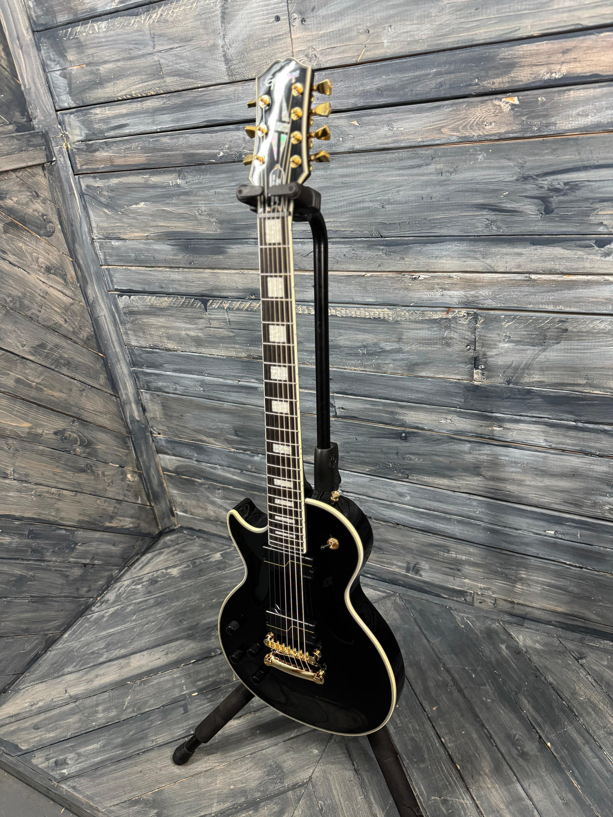 Black electric guitar on a stand against a wooden wall.