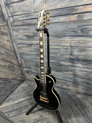 Black electric guitar on a stand against a wooden wall.