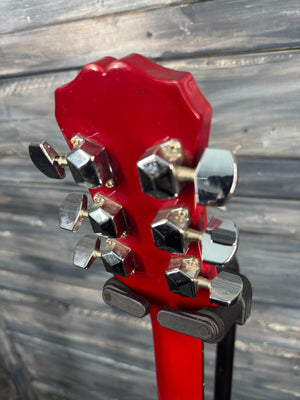 Close-up of a red guitar headstock with tuning pegs against a wooden background