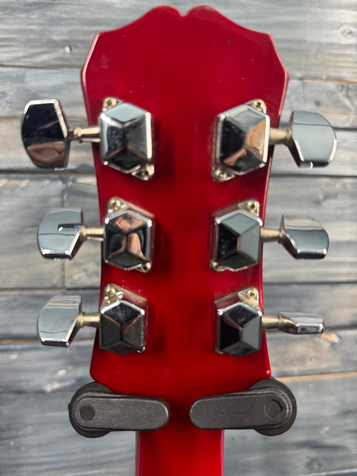 Close-up of a red guitar headstock with tuning pegs against a wooden background