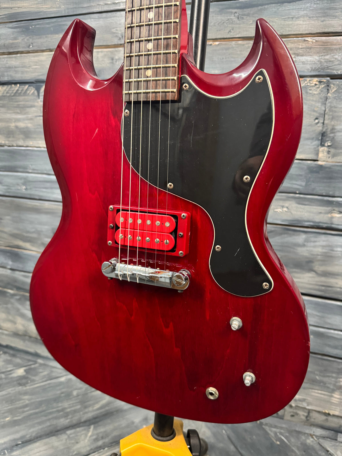 Red electric guitar with a black pickguard against a wooden background