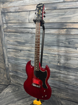 Red electric guitar leaning against a wooden wall