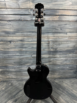 Black electric guitar on a stand against a wooden wall.