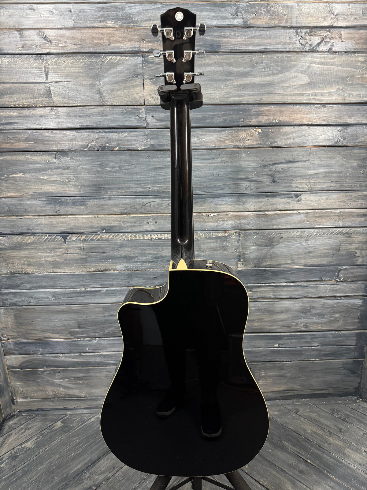 Black acoustic guitar leaning against a wooden wall