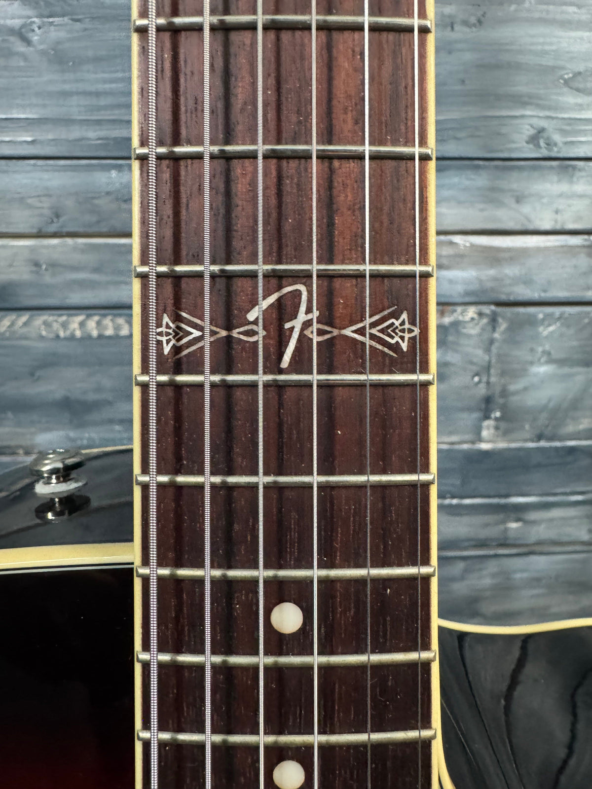 Close-up of a guitar neck with inlaid markers against a wooden background