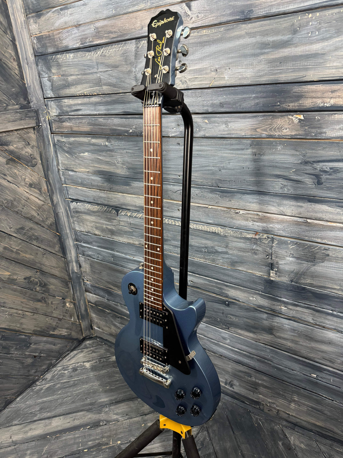 Blue electric guitar leaning against a wooden wall