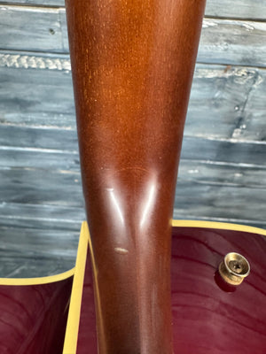 Close-up of a guitar's wooden neck with a metal tuning peg against a blurred wooden background.