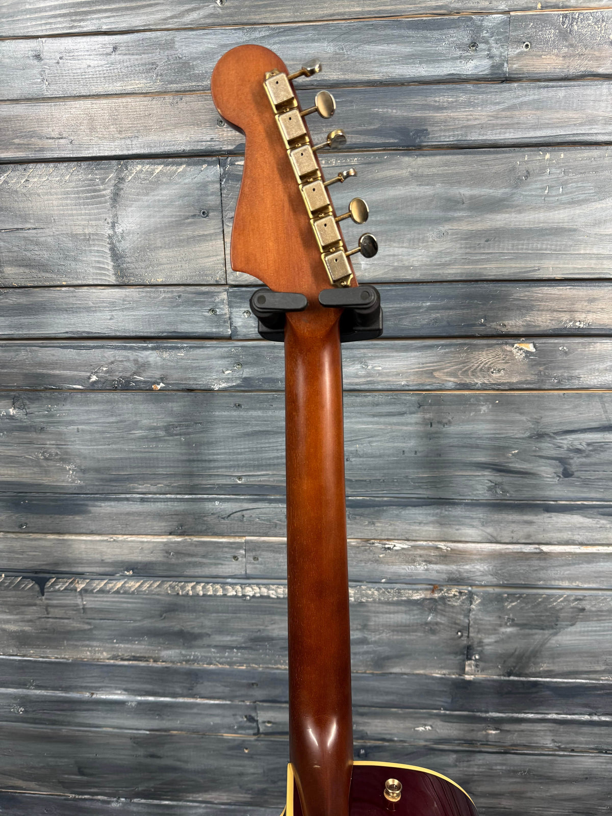 Guitar neck with wooden fretboard against a wooden panel background