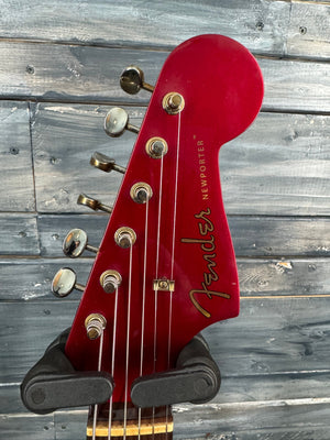 Red Fender bass guitar headstock against a wooden background
