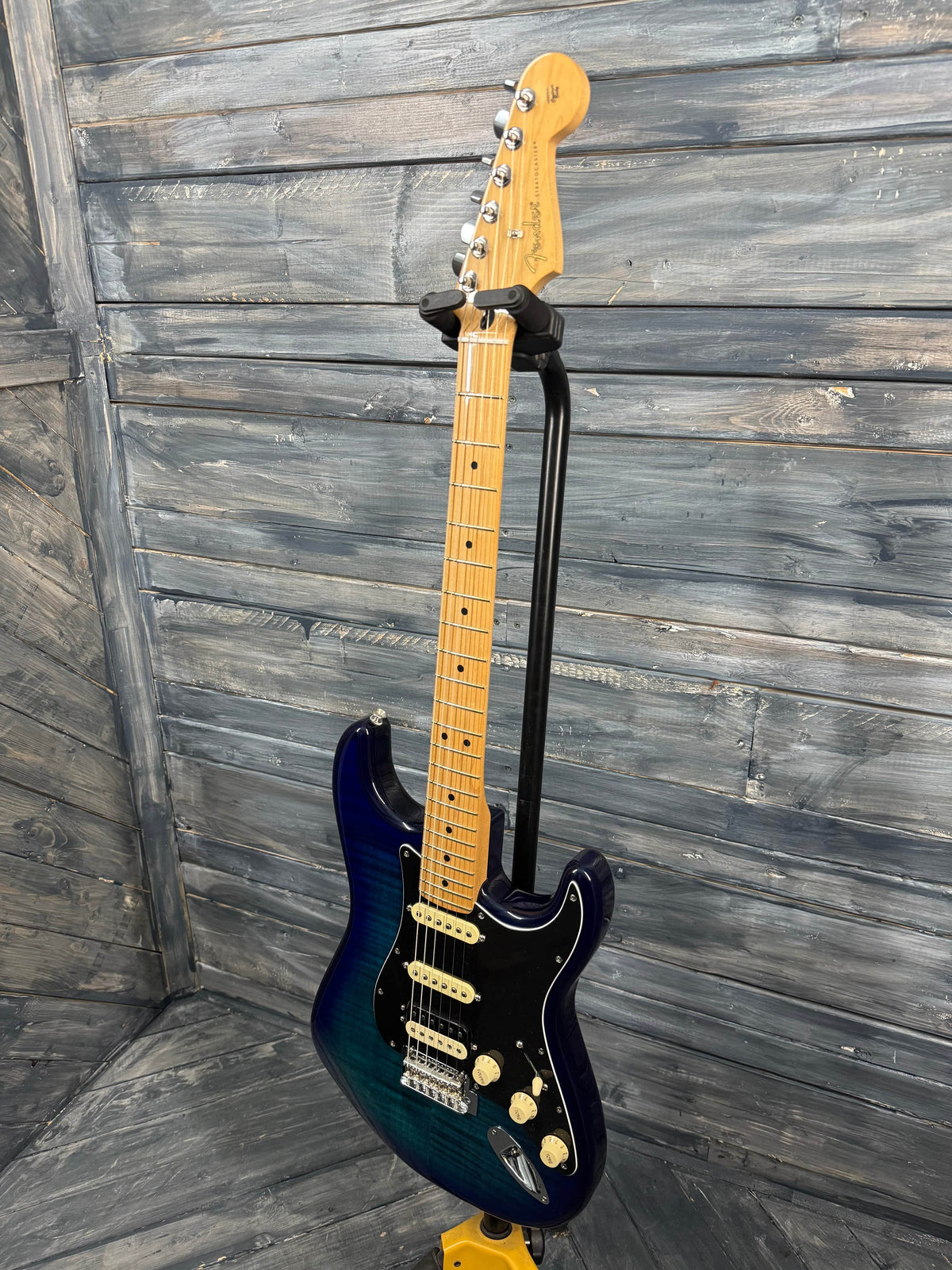 Blue electric guitar leaning against a wooden wall.