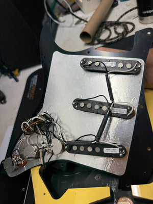 Guitar pickup assembly on a workbench with tools and parts in the background