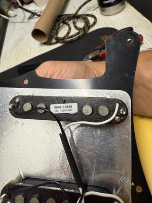 Guitar pickup with visible branding and model number on a workbench.