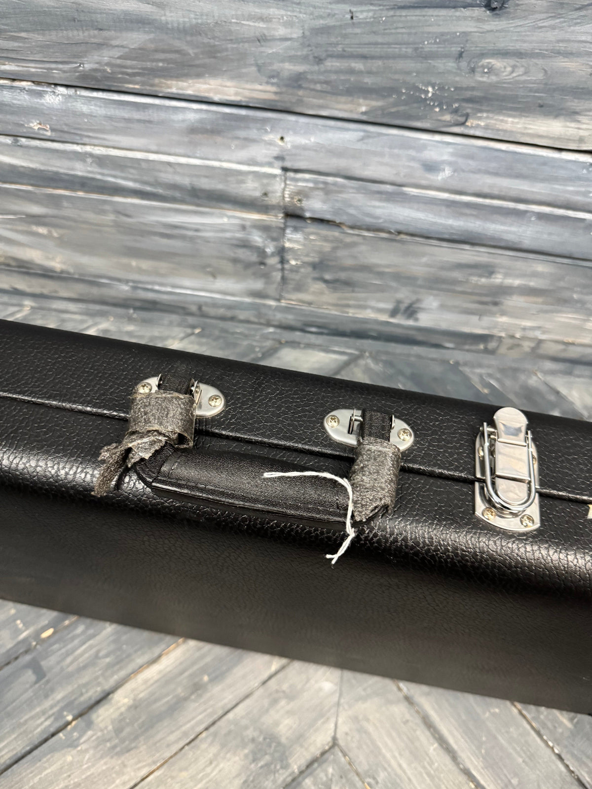 Black guitar case with silver latches on a wooden surface