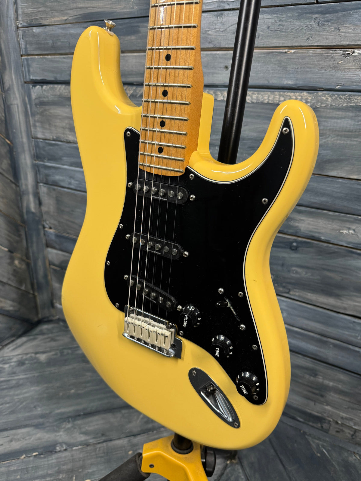 Yellow electric guitar with black pickguard on a wooden background