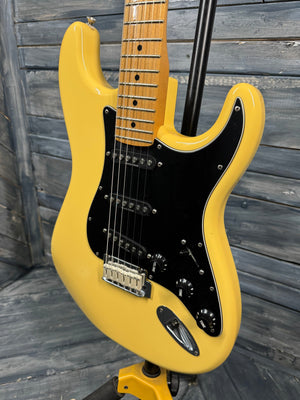 Yellow electric guitar with black pickguard on a wooden background
