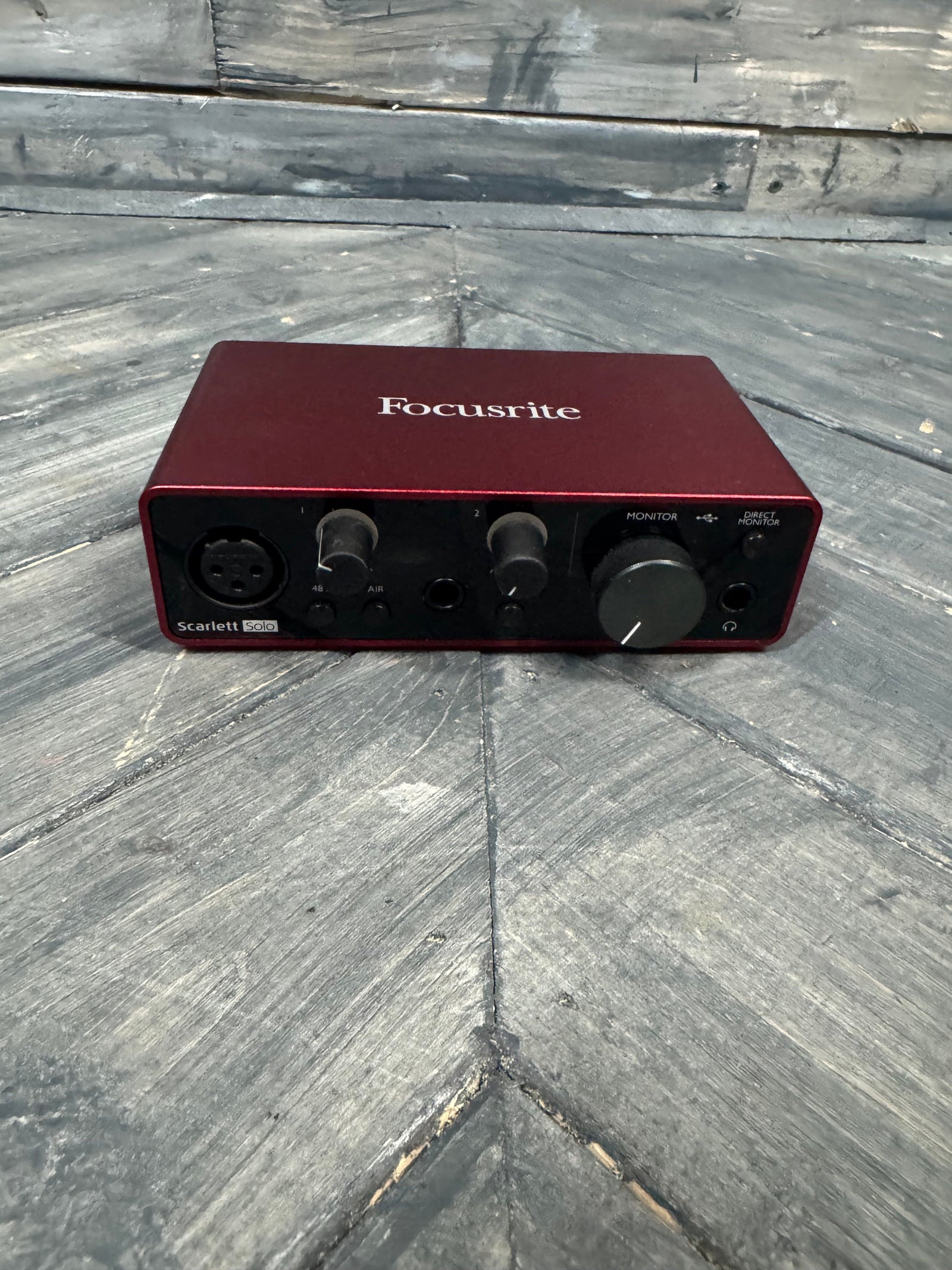 Red audio interface with knobs and ports on a gray tiled floor