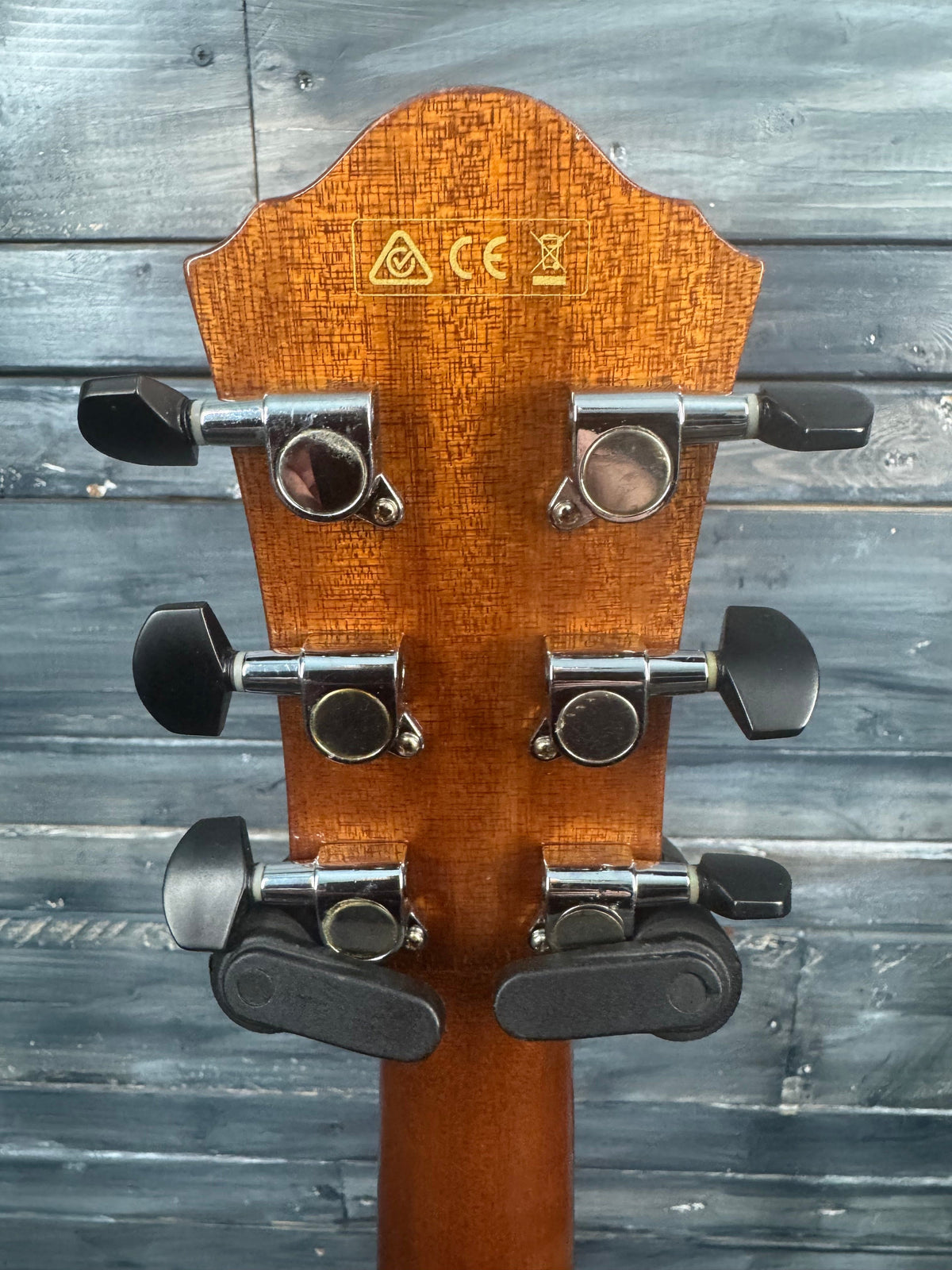 Close-up of a guitar headstock with tuning pegs against a wooden background
