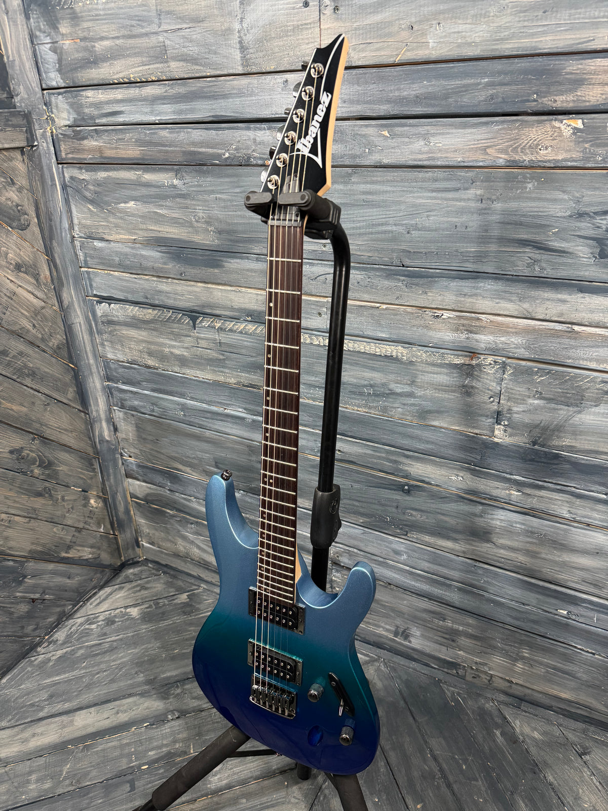 Blue electric guitar on a stand against a wooden background